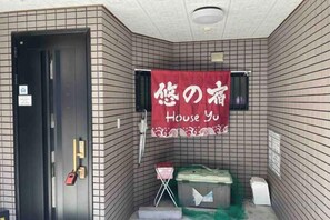 A corner of a room with a tiled wall, a black door, a red towel hanging, and a small table with a green container. - Younoyado (Osaka)