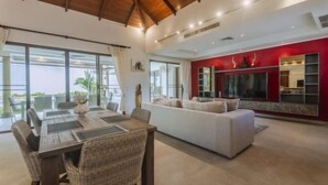 A spacious living area with a dining table and chairs, a white sofa, and a red accent wall. - Luxury 4Br Villa 5 Private Pool & Jacuzzi (Phuket)
