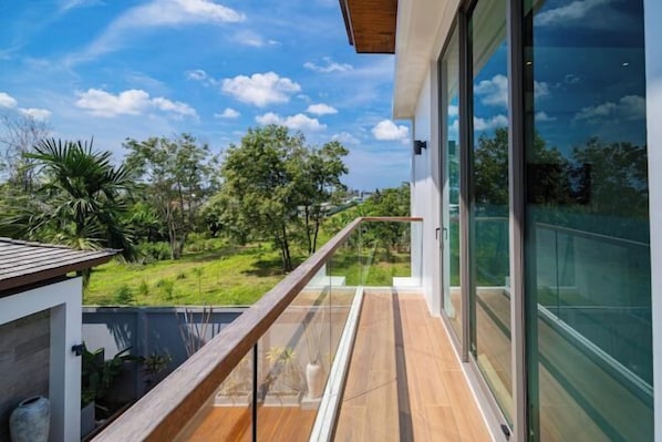 A modern balcony with glass doors, wooden flooring, and a view of a green landscape.