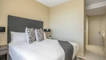 A neatly made bed with a grey headboard, two bedside lamps, and patterned pillows.