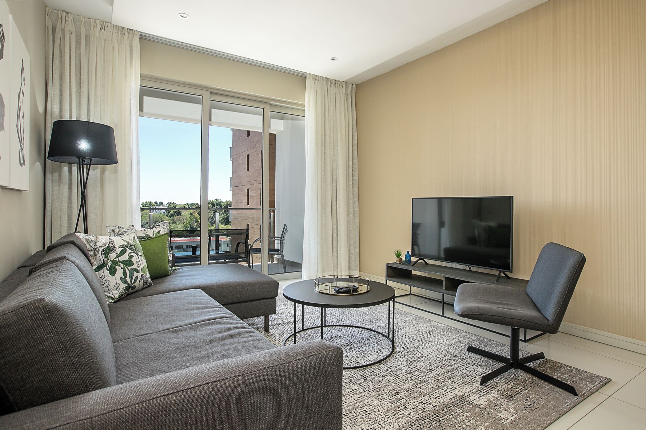 Una sala moderna con un sofá gris, una mesa redonda de centro, un televisor y una silla.