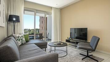 Una sala moderna con un sofá gris, una mesa redonda de centro, un televisor y una silla.