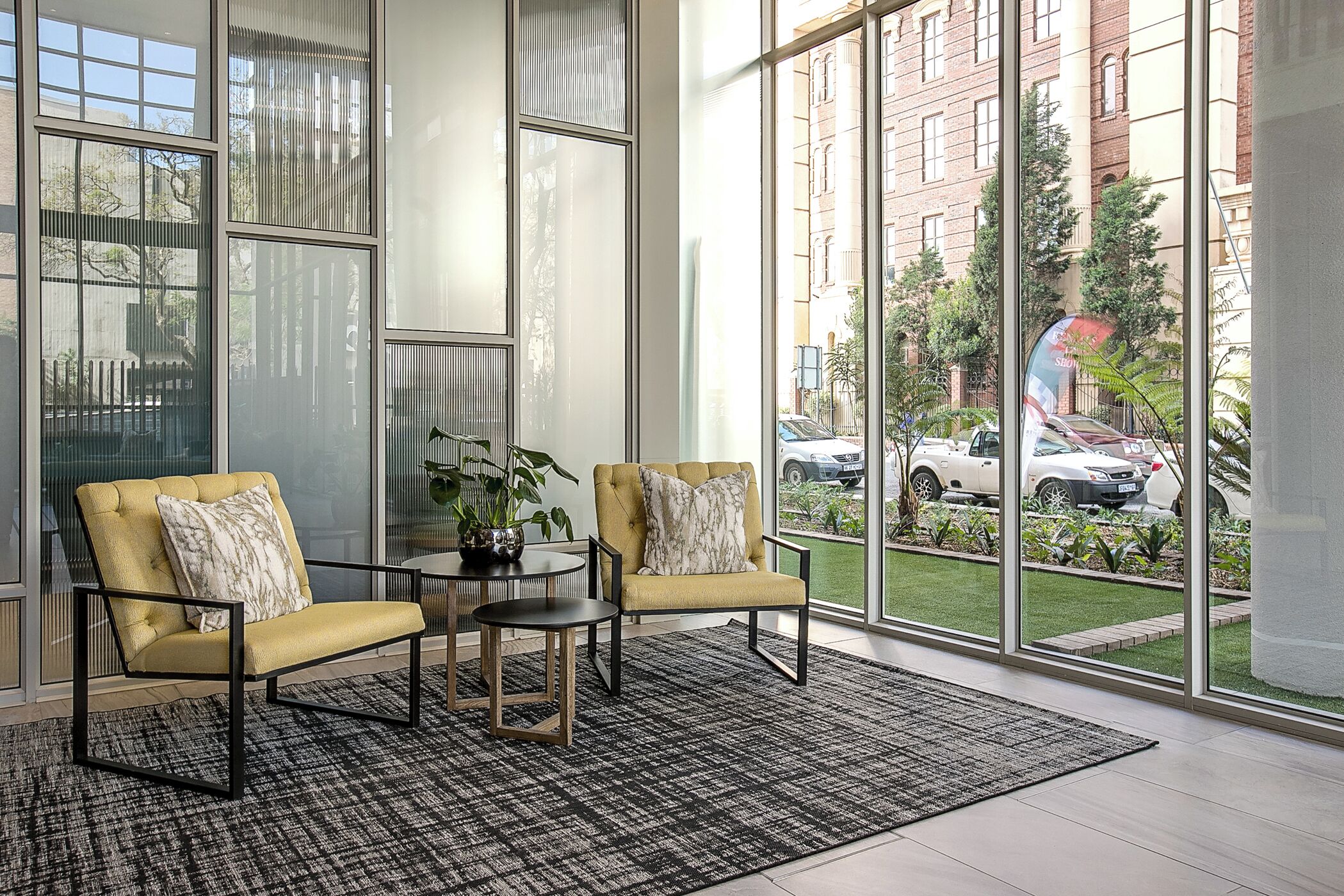 Una habitación moderna con ventanas amplias, dos sillones amarillos, una mesita y una planta en maceta.