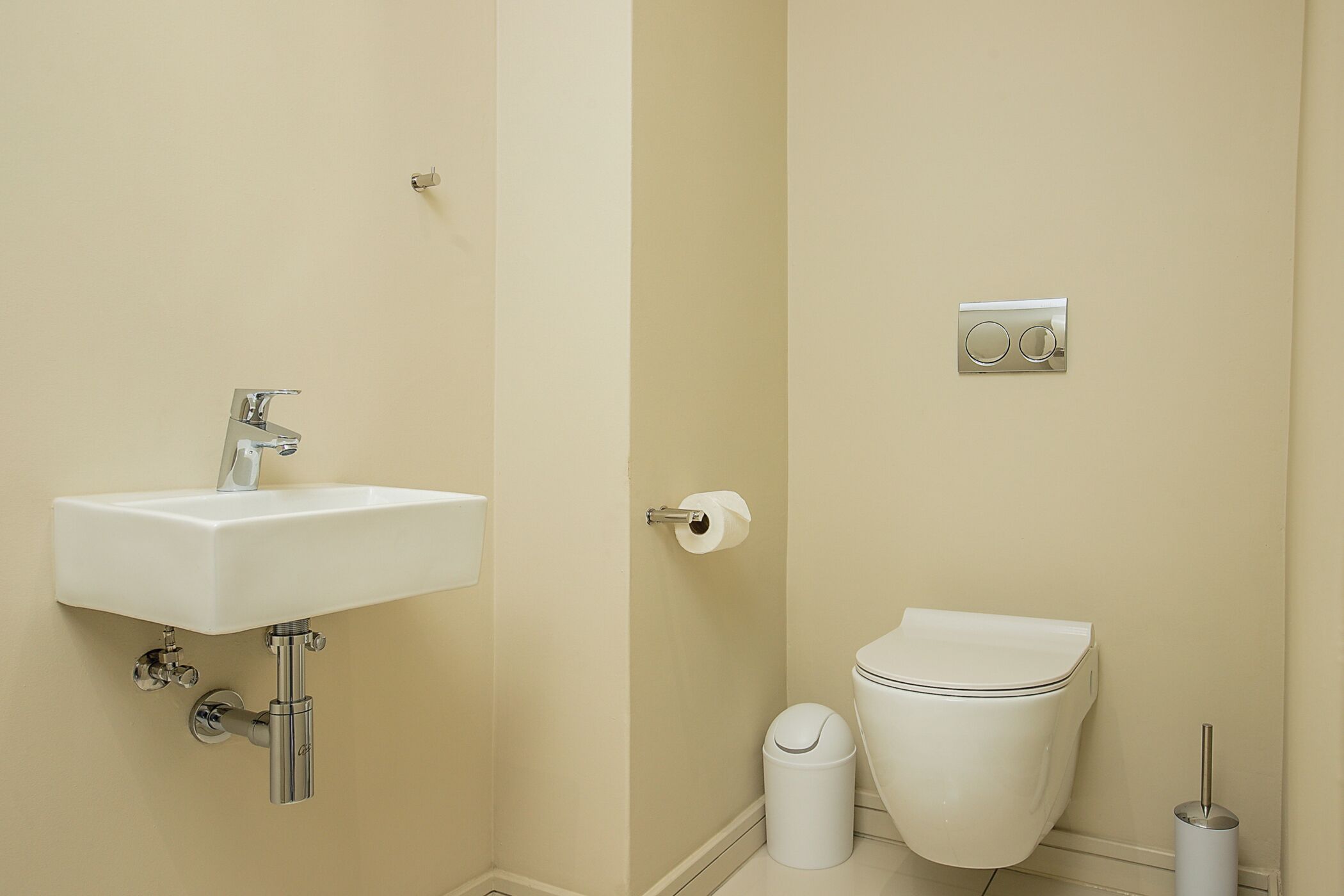 A bathroom with a white sink, toilet, and trash bin.