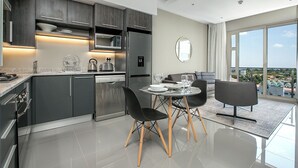 Una cocina moderna con armarios oscuros, electrodomésticos de acero inoxidable y un comedor con mesa de vidrio y sillas negras.