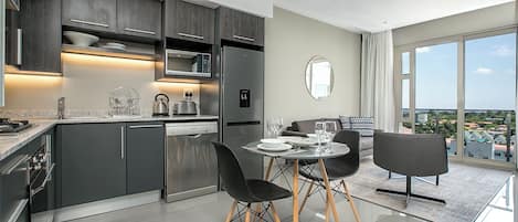 A modern kitchen with dark cabinets, stainless steel appliances, and a dining area with a glass table and black chairs.