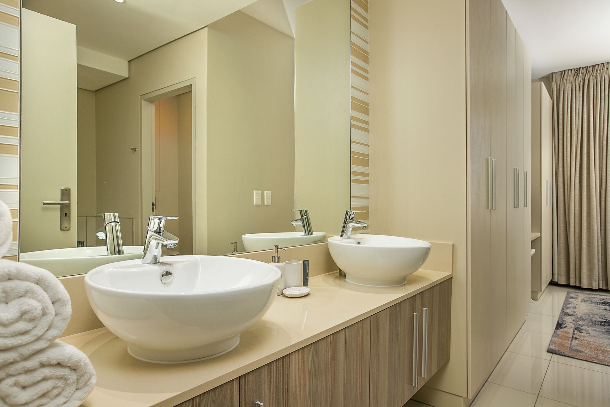 A modern bathroom with two large sinks, a mirror, and wooden cabinetry.