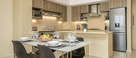 Una cocina moderna con armarios de madera, un refrigerador de acero inoxidable y un comedor con mesa dispuesta para cuatro.