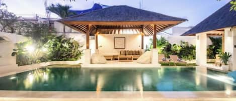 A pool area with a covered seating area and lounge chairs.