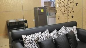 A living area with a sofa, pillows, a small table, and a refrigerator. - HapiBelles Staycation Trees Residence Tower 8 (Quezon City)
