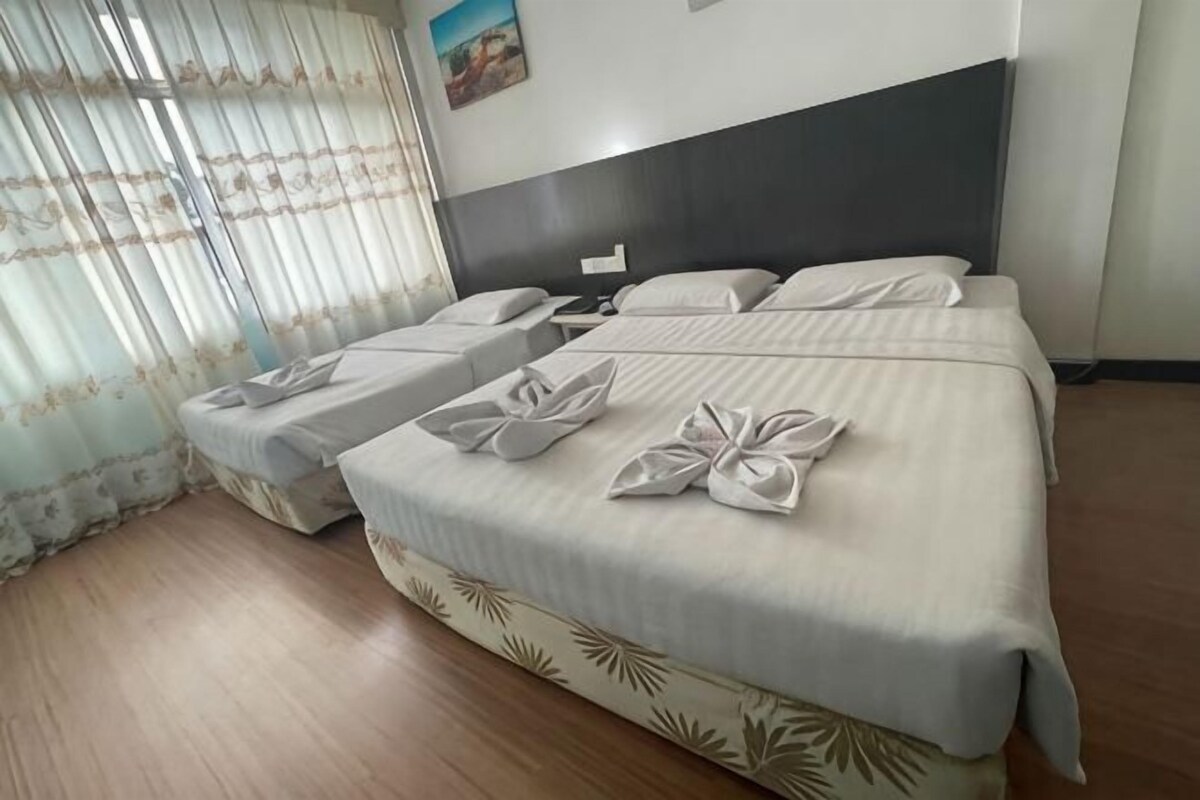 Una habitación de hotel con una cama grande, dos camas más pequeñas y suelo de madera.
