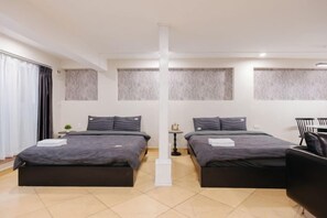 Una habitación de hotel moderna con dos camas, una mesita pequeña, una silla y un amplio ventanal con cortinas.