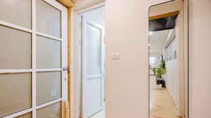 Un pasillo con una puerta corredera de vidrio que da a una habitación, un espejo en la pared y una planta en maceta al fondo.