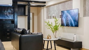 Una sala de estar moderna con un sofá de cuero negro, una mesita redonda y un televisor de pantalla plana montado en la pared.