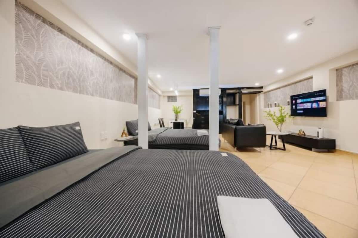 A modern hotel room with a large bed, a sofa, a TV, and a desk.