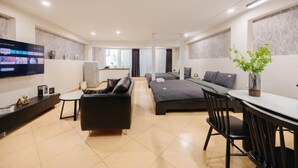 Habitación de hotel moderna con televisión de pantalla plana, sofá, cama, mesa de comedor y una planta pequeña.