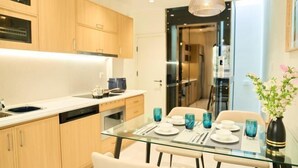 A modern kitchen with wooden cabinets, a glass dining table set for four, and a vase with flowers on the table. - Home by La Sinfonía Trieu Viet Vuong (Hanoi)
