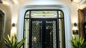 A hotel entrance with a decorative glass door, a sign with the number 6, and two potted plants on either side. - Home by La Sinfonía Trieu Viet Vuong (Hanoi)