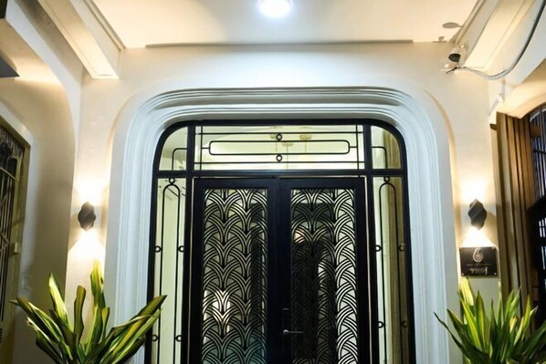 A hotel entrance with a decorative glass door, a sign with the number 6, and two potted plants on either side. - Home by La Sinfonía Trieu Viet Vuong (Hanoi)