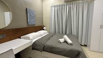 A hotel room with a bed, a bedside table, a mirror, a wall-mounted air conditioner, and a curtain.