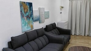 Egy modern nappali, szürke színű kanapéval, kerek dohányasztallal és a falon elhelyezett műalkotásokkal.