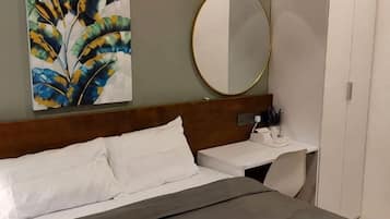 A hotel room with a bed, a bedside table, a mirror, and a wall-mounted artwork.