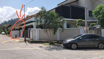 A residential street with a parked car, a house with a white facade, and a small tree.