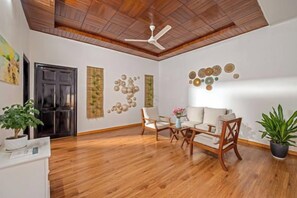 A room with a ceiling fan, wooden flooring, a sofa, chairs, and decorative wall art. - Mango House 5Br 7 BEDS pool villa (Da Nang)