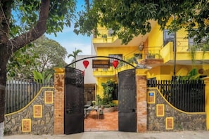 A gated entrance with a stone wall, a yellow building with a balcony, and a red heart decoration. - Mango House 5Br 7 BEDS pool villa (Da Nang)