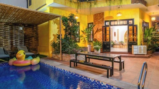 Una piscina interior con borde de azulejos, rodeada por una zona de patio con una banca y sillones de descanso.
