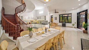 Un comedor amplio con una mesa larga dispuesta para seis comensales, una escalera de madera y una cocina al fondo.