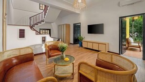 Amplia sala de estar con escalera, televisor de pantalla plana, muebles de mimbre y vista a la vegetación a través de una puerta de vidrio.