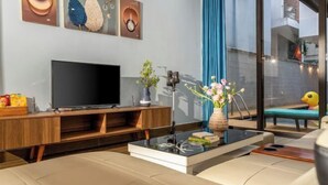 Een moderne woonkamer met een flatscreen-televisie, een houten tv-meubel en een glazen salontafel met boeken en een bloevas.