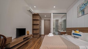Een moderne hotelkamer met een houten vloer, een bed met een witte dekbedovertrek, een televisie op een houten dressoir en een kast met meerdere planken.