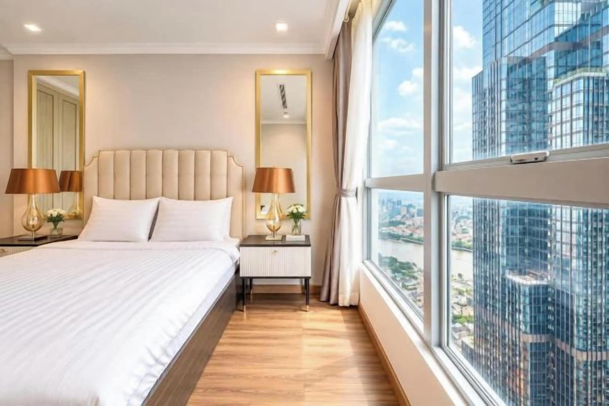 Een hotelkamer met een groot bed, bedlampen, een nachtkastje, een raam met uitzicht over de stad en een spiegel.