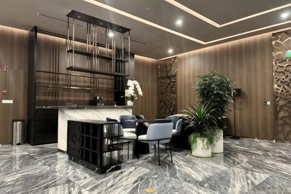 Un vestíbulo moderno con suelo de mármol, una recepción, zona de estar y plantas decorativas.