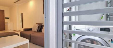 A modern room with a sofa, a small table, and a washing machine visible through a glass door.