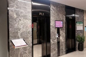 L’entrée d’un hôtel, avec deux ascenseurs, un écran numérique et un panneau indiquant l’emplacement d’un centre d’affaires.