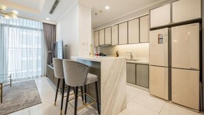 A modern kitchen with a marble island, bar stools, and built-in appliances. - Golden Grand Landmark (Ho Chi Minh City)