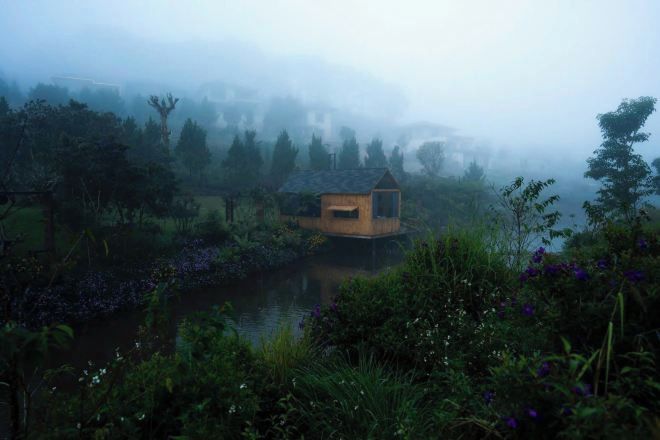 Una cabaña rústica junto a un lago, rodeada de abundante vegetación.