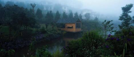 A rustic cabin by a lake surrounded by dense foliage.