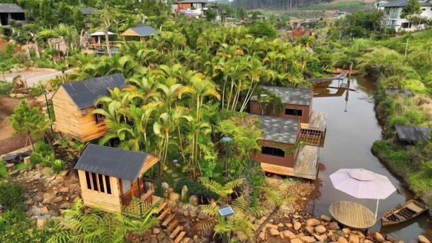 A rural village with wooden houses surrounded by lush greenery and a small waterway. - The Village Resort in the Painting, Bao Loc (Bao Lam District)