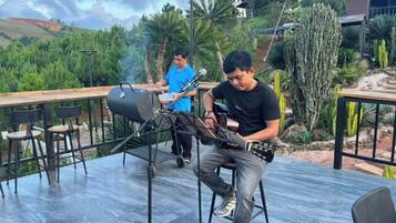 Una persona tocant la guitarra en un escenari a l'aire lliure, amb una barbacoa de fons.