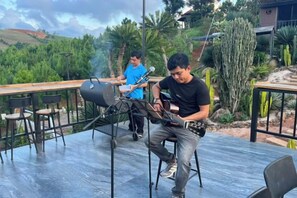 Een persoon speelt gitaar op een open podium, met een barbecuegrill op de achtergrond.
