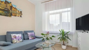 Una sala de estar con un sofá, una mesa de centro de cristal, una planta en maceta y un televisor.