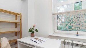 Un escritorio blanco con una planta y una revista abierta, una estantería de madera y un radiador.
