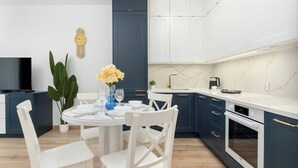Uma cozinha moderna com armários brancos, forno embutido e área de refeições com mesa redonda e cadeiras brancas.