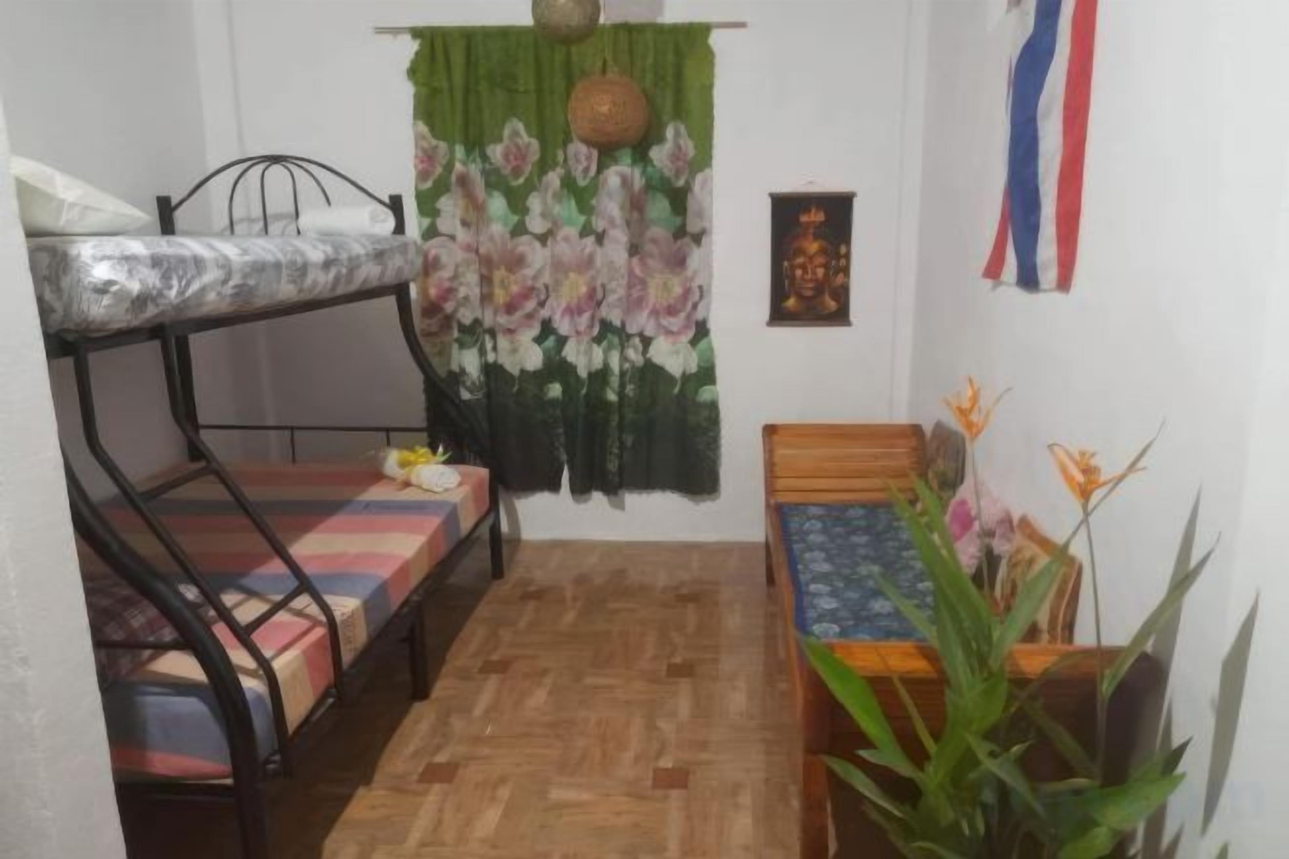 A small room with a bunk bed, a single bed, a wooden table, and a potted plant.