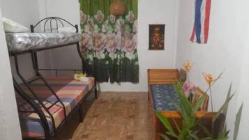 A small room with a bunk bed, a single bed, a wooden table, and a potted plant.