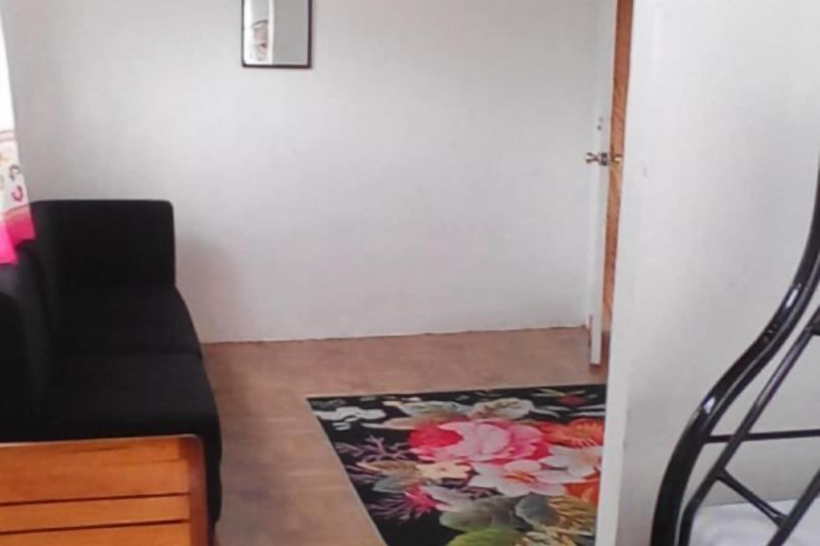 A room with a wooden bench, a black chair, and a floral rug.